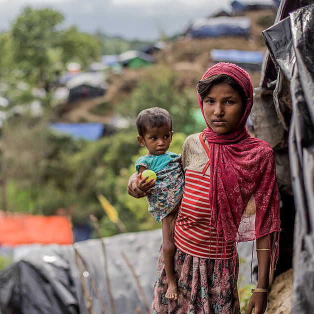 Hamida steht mit ihrer kleinen Schwester Bushra auf dem Arm vor einer selbstgebauten Unterkunft im Flüchtlingscamp in Bangladesch