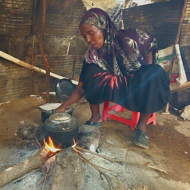 Eine Frau in ärmlichen Verhältnissen hockt vor ihrer provisorischen Küche vor ihrem offenen Feuer und kocht Essen für ihre Familie.