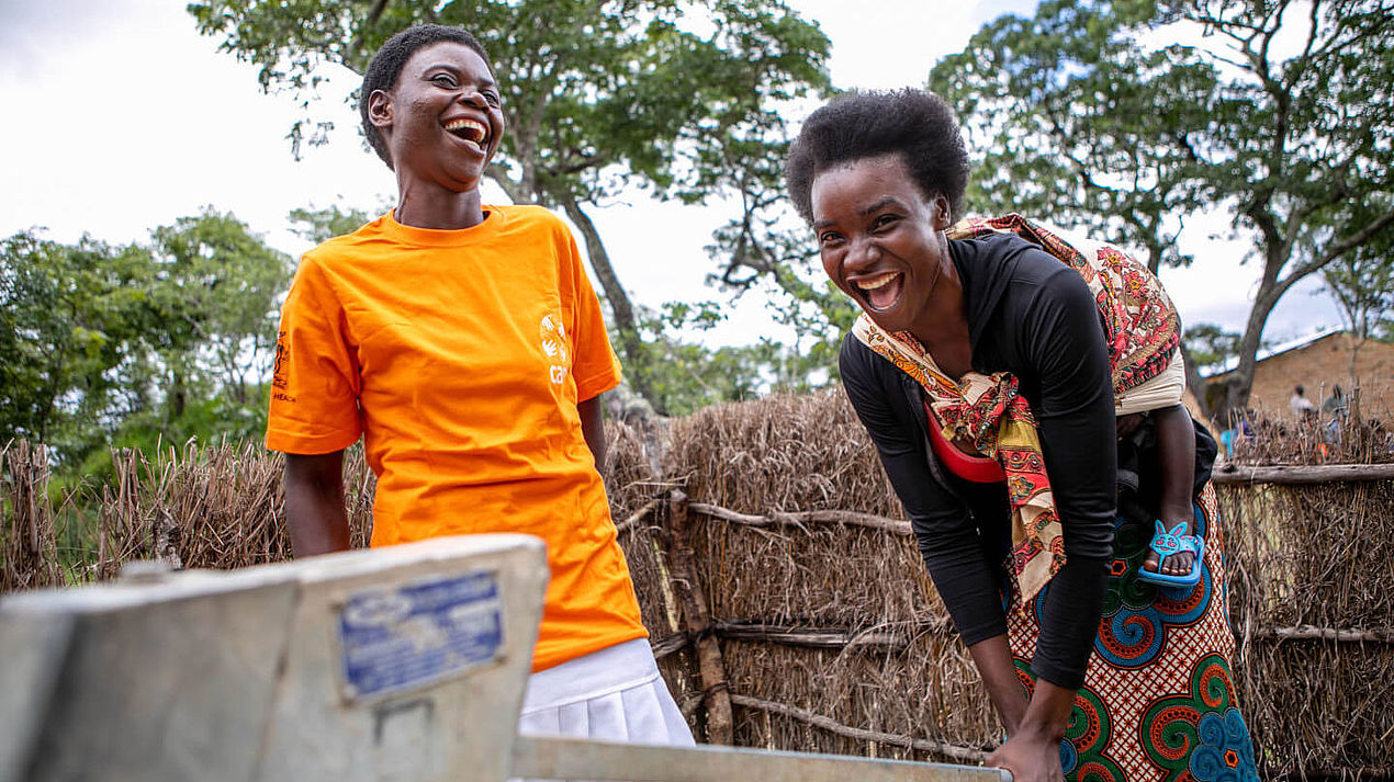 Zwei Frauen in Sambia stehen an einem Brunnen und lachen
