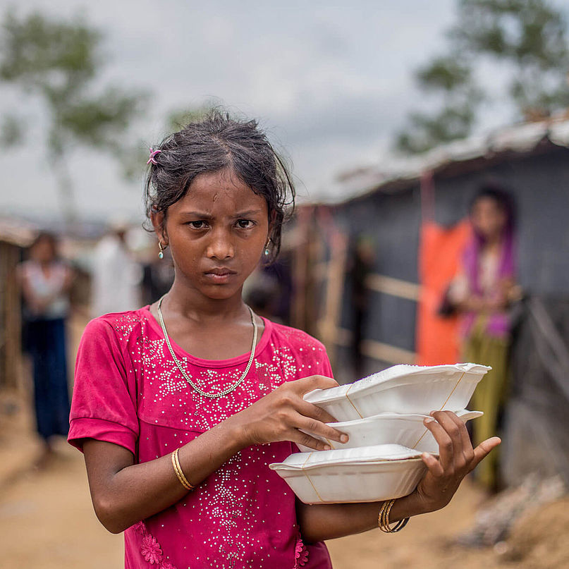 Ein Mädchen steht mit Nahrungsmitteln im Flüchtlingscamp 