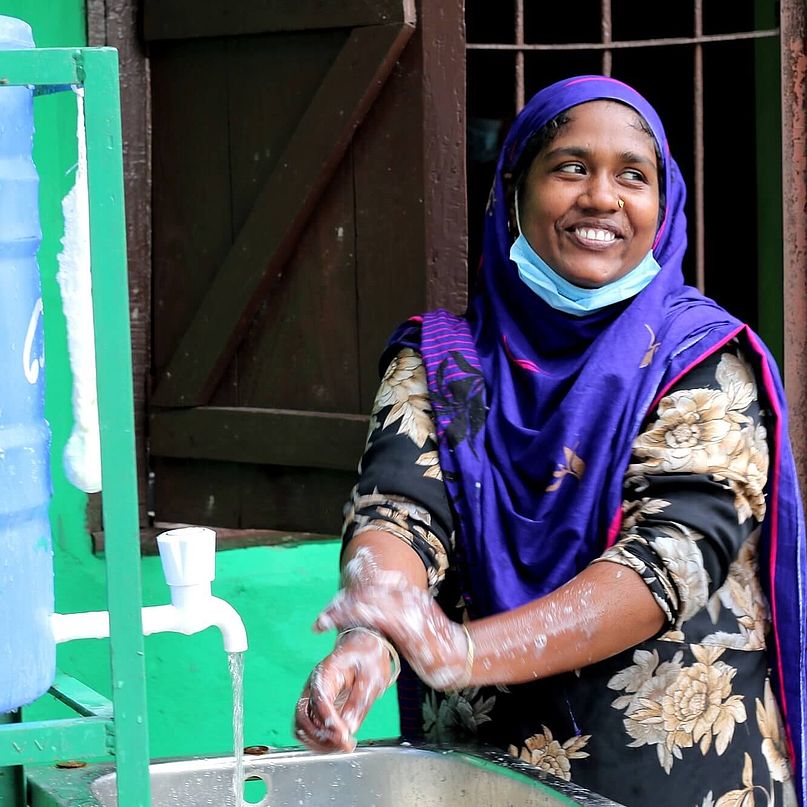 Frau wäscht ihre Hände an einer Handwaschstation in Bangladesch