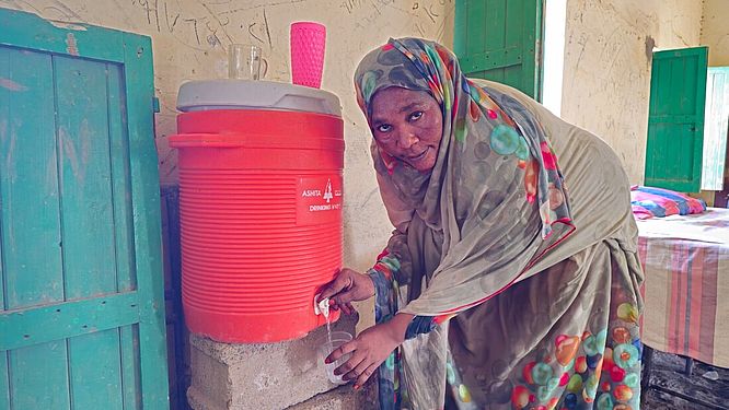 Eine Frau füllt einen Becher an einem Wasserspender in einer Notunterkunft