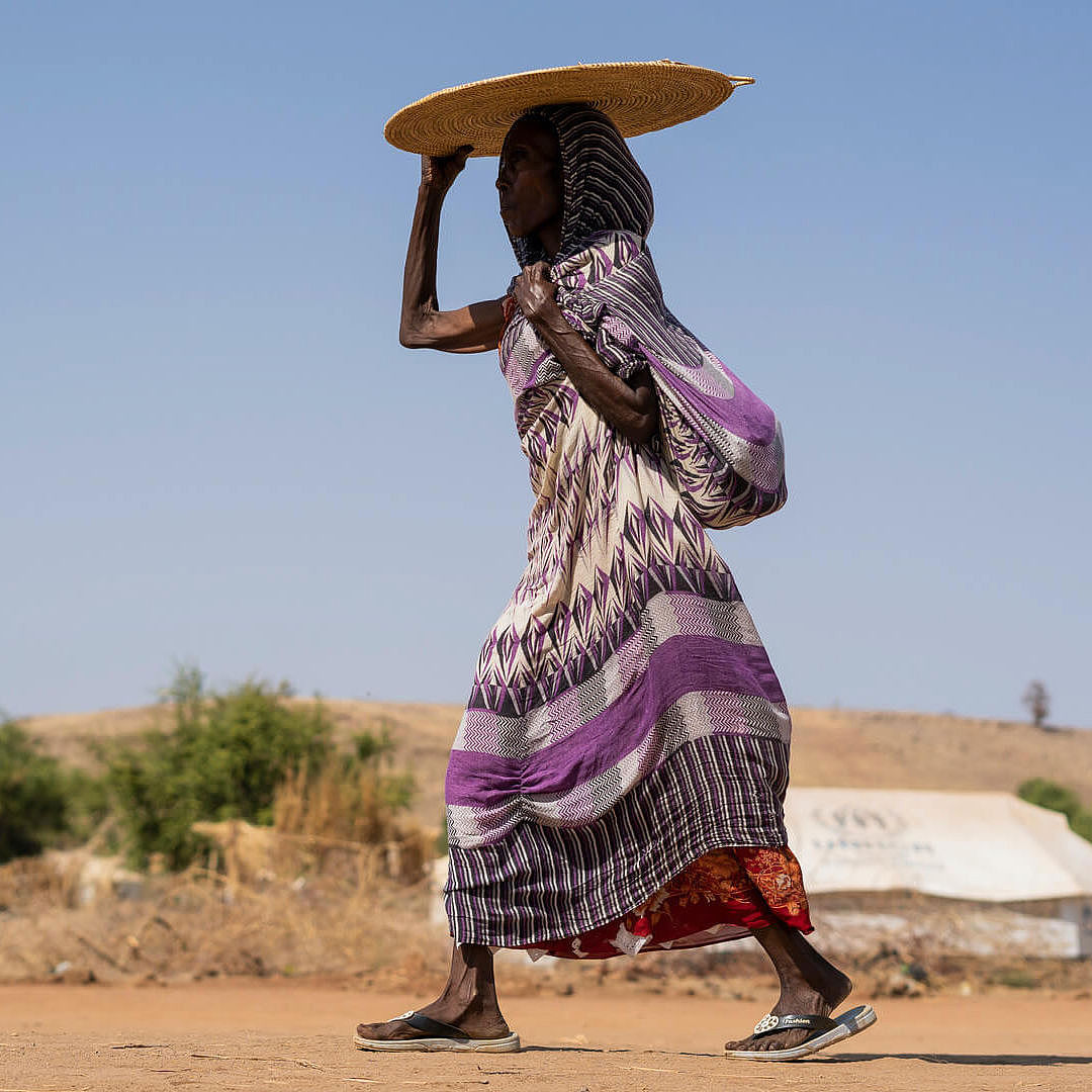 Eine Frau geht durch ein Flüchtlingscamp und hält sich etwas über den Kopf, um Schatten zu spenden