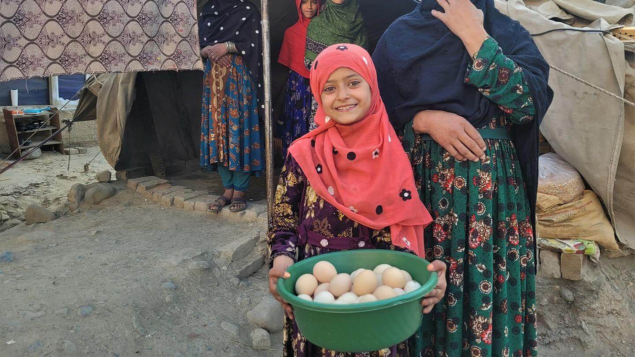 Ein Mädchen mit pinkem Kopftuch hält einen Korbmit Eiern und schaut in die Kamera.