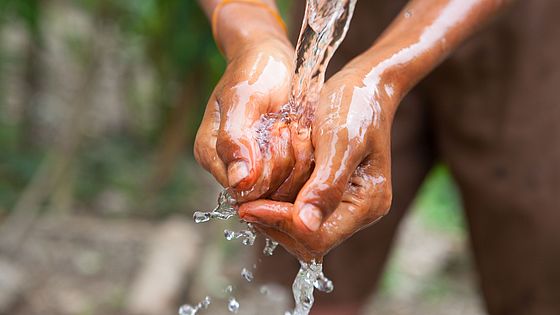 Ein Junge wäscht seine Hände an einem Bambusrohr.