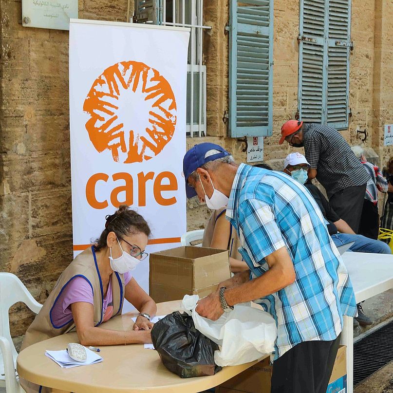 Eine CARE-Mitarbeiterin verteilt Hilfsgüter an einen älteren Herrn