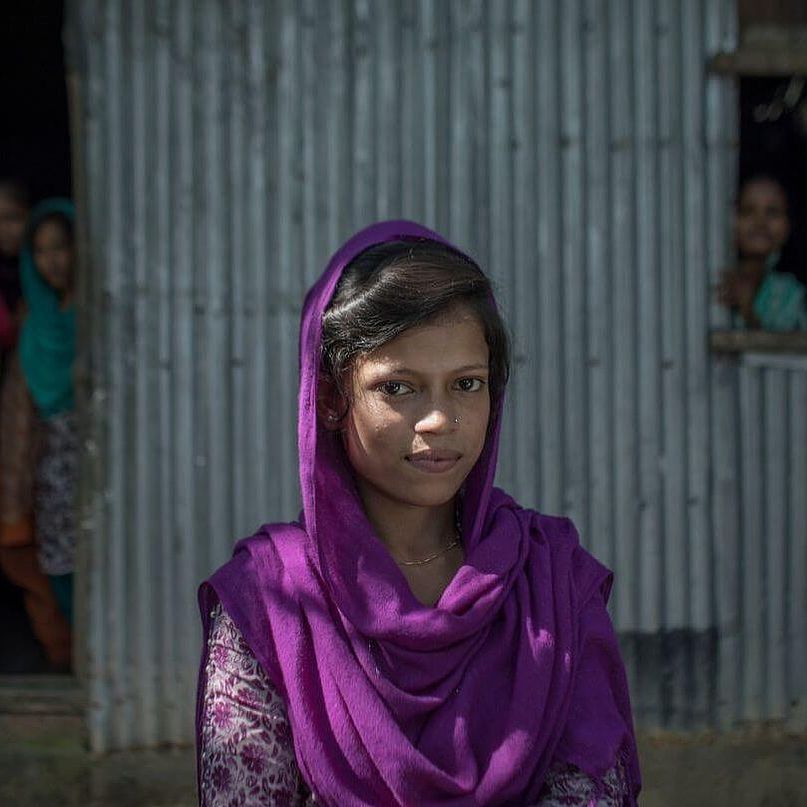 Junges Mädchen aus Bangladesh steht vor einem Haus.