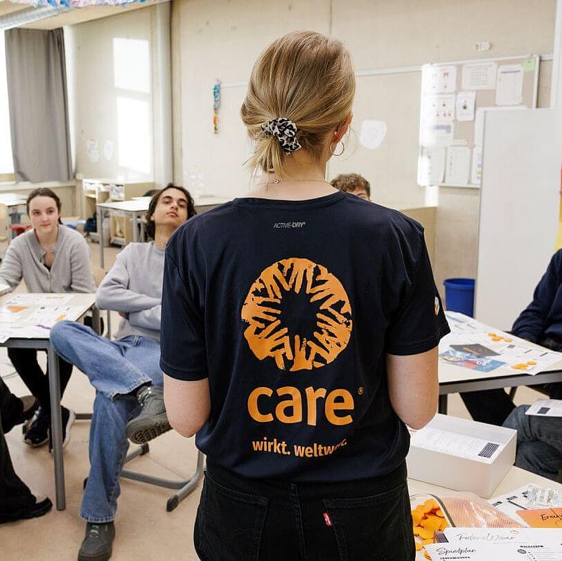 Eine CARE-Mitarbeiterin erlaeutert das Planspiel einer Gruppe Schueler:innen