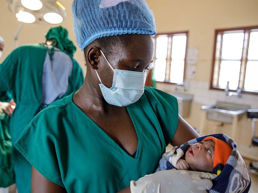 Hebamme aus Uganda haelt ein Neugeborenes nach der Entbindung in den Haenden.