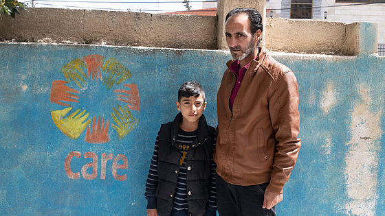 Mohammad und sein Vater Otaibi stehen vor dem CARE-Symbol