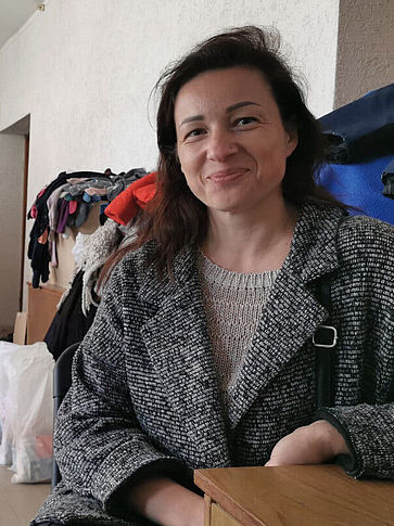 Olena aus der Ukraine sitzt an einem Tisch und blickt in die Kamera.
