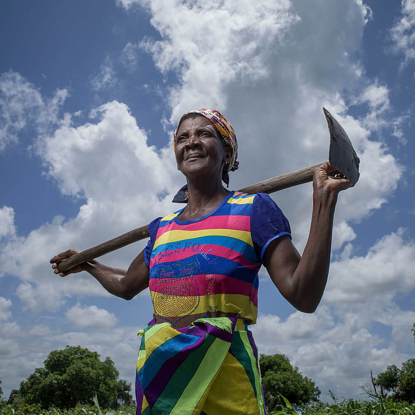 Die 70-jährige Mantando Joan aus Mosambik steht mit Pflügwerkzeug auf einem Feld