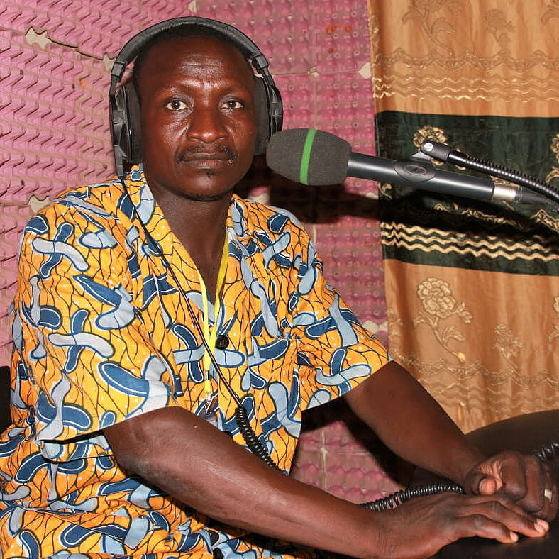 Ein Radiomoderator in einem bunten Hemd sitzt mit Kopfhörern vor einem Mikrofon im Studio des Radiosenders NYAA FM.