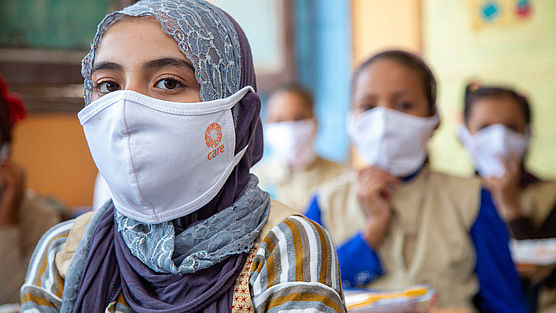 Ein Mädchen sitzt in einer Schulklasse und trägt eine Schutzmaske