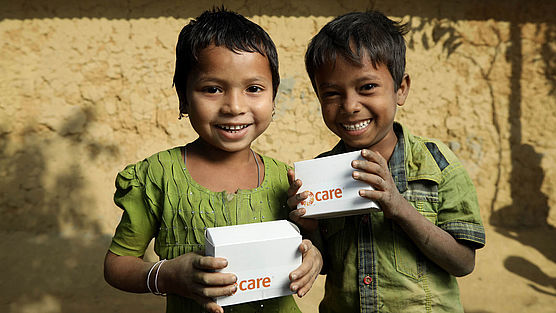 Geflüchtete Kinder in Bangladesch halten kleine CARE-Pakete in den Hönden und lachen