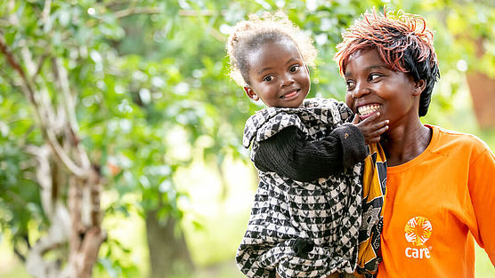 Eine CARE-Helferin in Sambia hält lächelnd ein Mädchen auf dem Arm