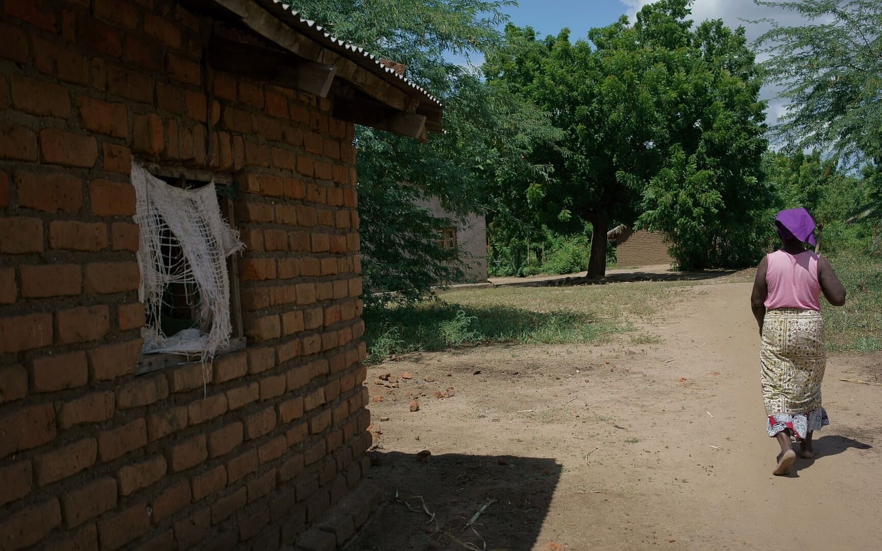 Rose aus Malawi geht an ihrem Steinhaus vorbei, der Vorhang ist eingerissen