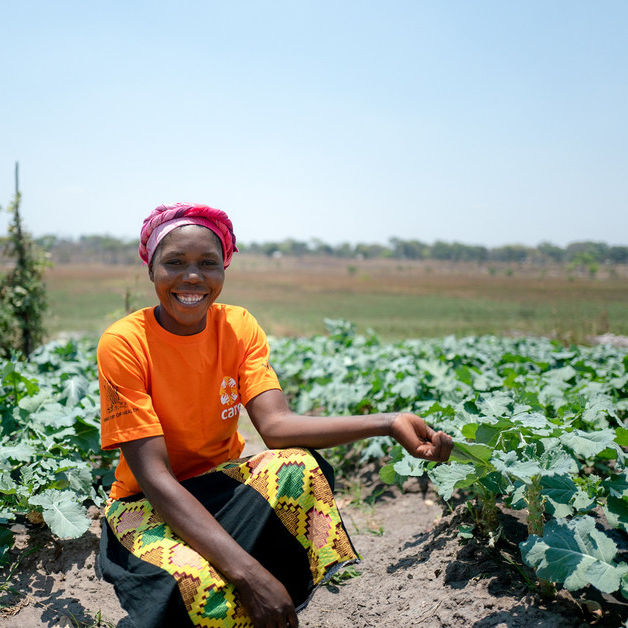 Eine CARE-Helferin in Sambia sitzt in einem Gemüsegarten