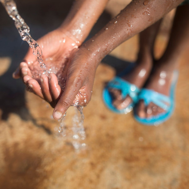 Ein Mädchen hält ihre Hände vor einen Wasserhahn, aus dem sauberes Wasser fließt
