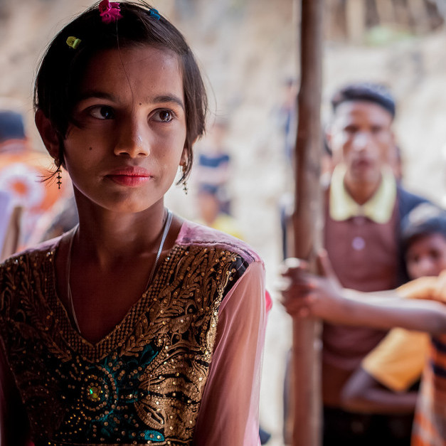 Ein Mädchen aus Bangladesch, im Hintergrund stehen junge Männer