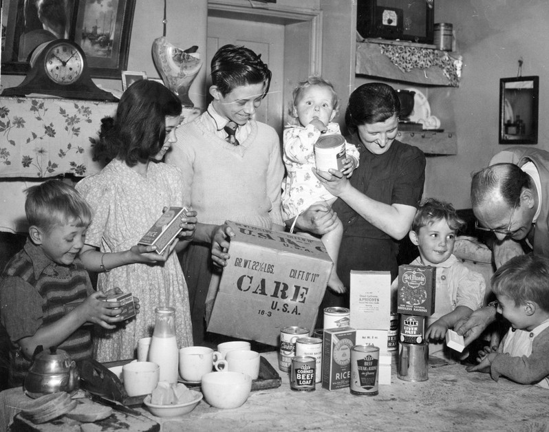 Eine Familie in der Nachkriegszeit packt ein CARE-Paket aus